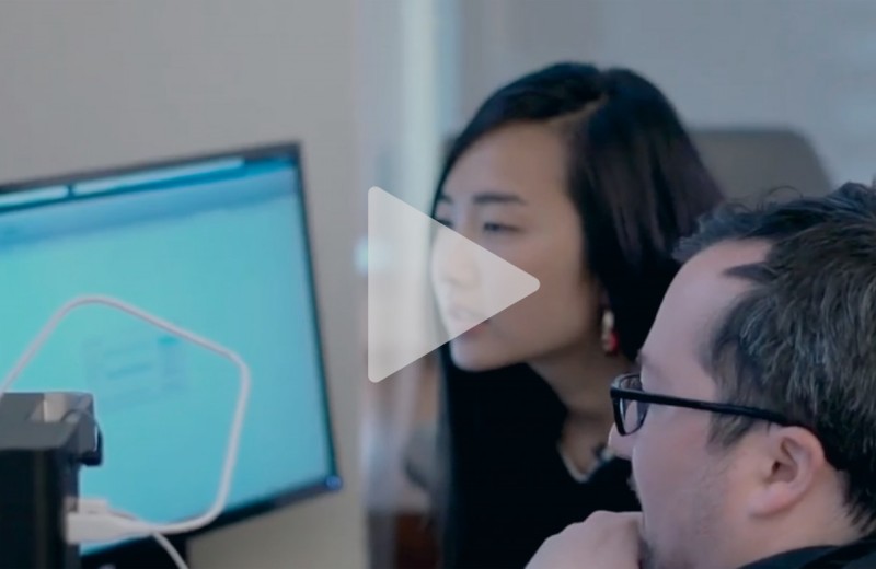 Image of two people looking at a computer screen with a play button overlayed